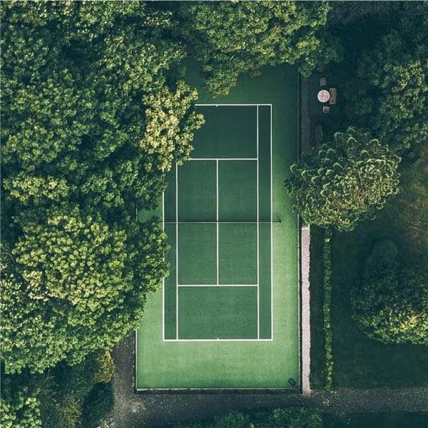 Tennis court Birds View flyover with green trees below slightly covering a tennis court
